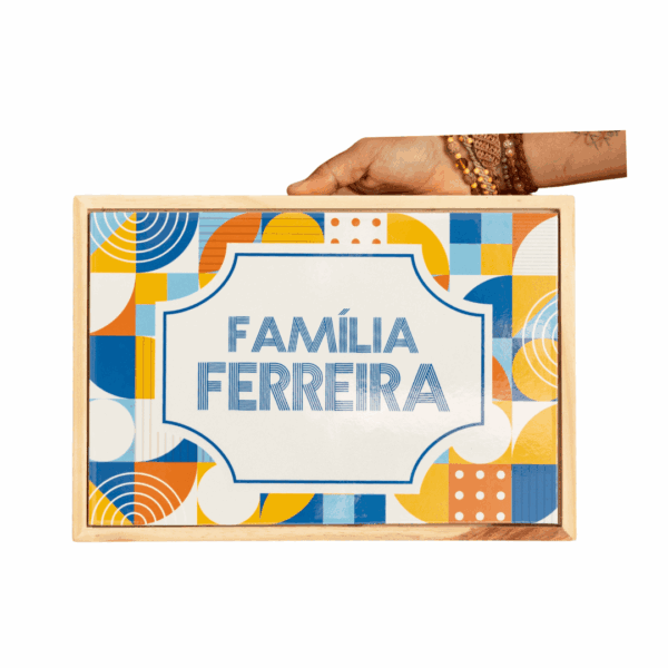 Mão segurando moldura de madeira com azulejo personalizado Família Ferreira em estampa geométrica colorida