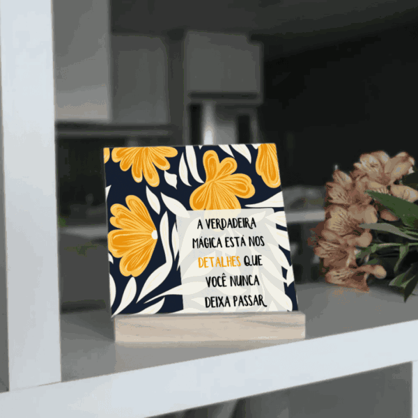Azulejo floral azul e amarelo com frase sobre gratidão, em base de madeira na estante