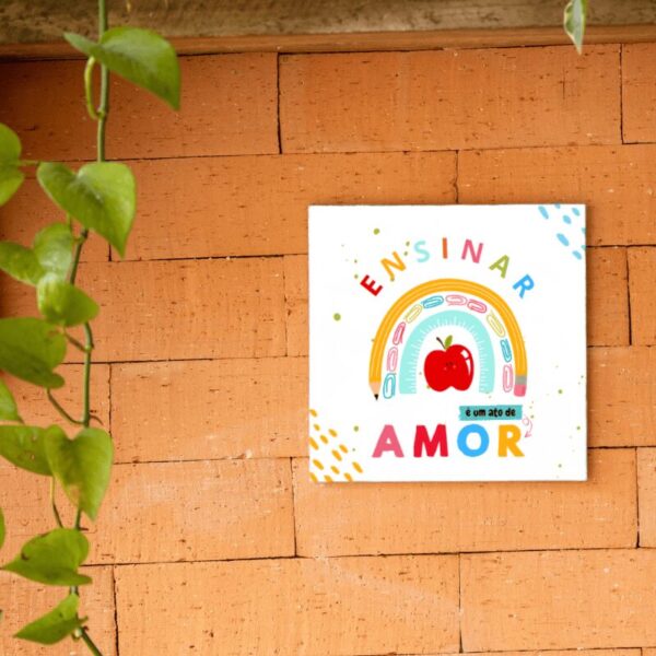 Azulejo decorativo Ensinar é um Ato de Amor pendurado na parede de tijolos