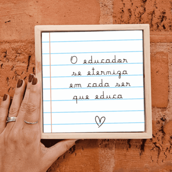 Mão segurando o azulejo O Educador se Eterniza em Cada Ser que Educa com moldura de madeira