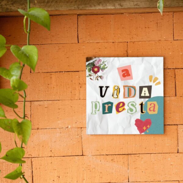 Azulejo decorativo A Vida Presta com letras de recorte coloridas, pendurado na parede de tijolos