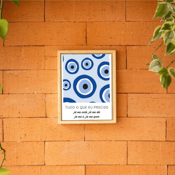 Azulejo retangular com olhos gregos azuis e frase, em moldura de madeira na parede de tijolos
