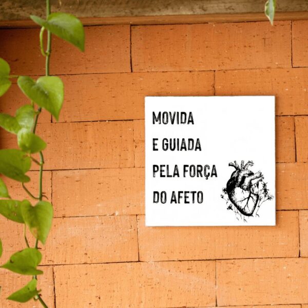 Azulejo Movida e Guiada pela Força do Afeto com coração ilustrado, pendurado na parede de tijolos