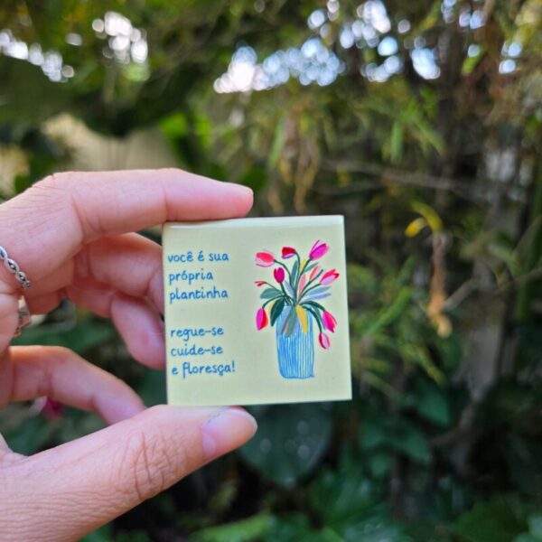 Mão segurando o mini azulejo com ímã da plantinha