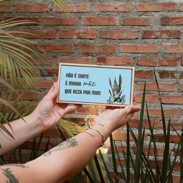 Mãos segurando uma plaquinha de azulejo com frase
