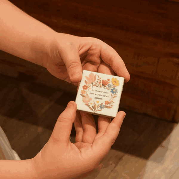 Mãos segurando ímã 5x5 em mini azulejo com coroa de flores e frase